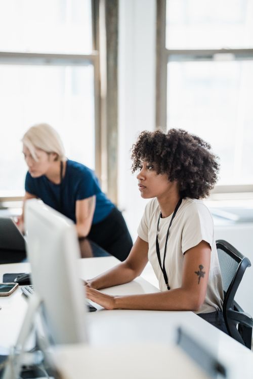 Free Two women working together in a modern, bright office setting, showcasing teamwork and collaboration. Stock Photo