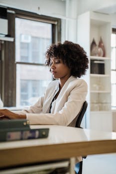 A young professional woman concentrating on her laptop in a bright, contemporary office setting.