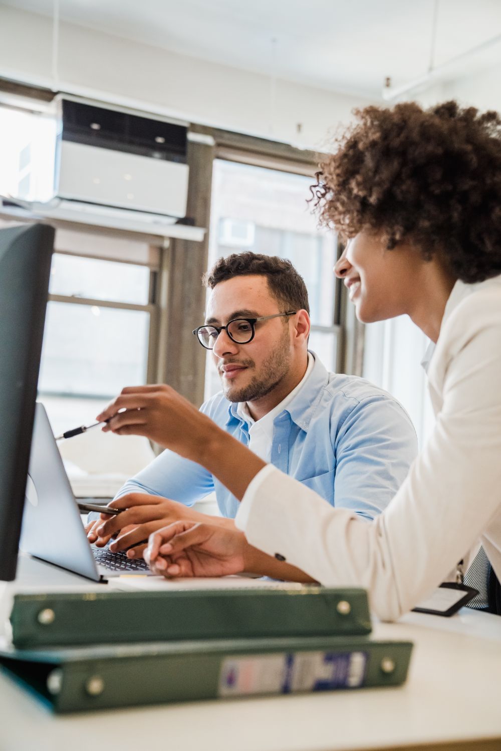 Two colleagues leaning over the same screen, one pointing something out. Photo by Mizuno K on Pexels