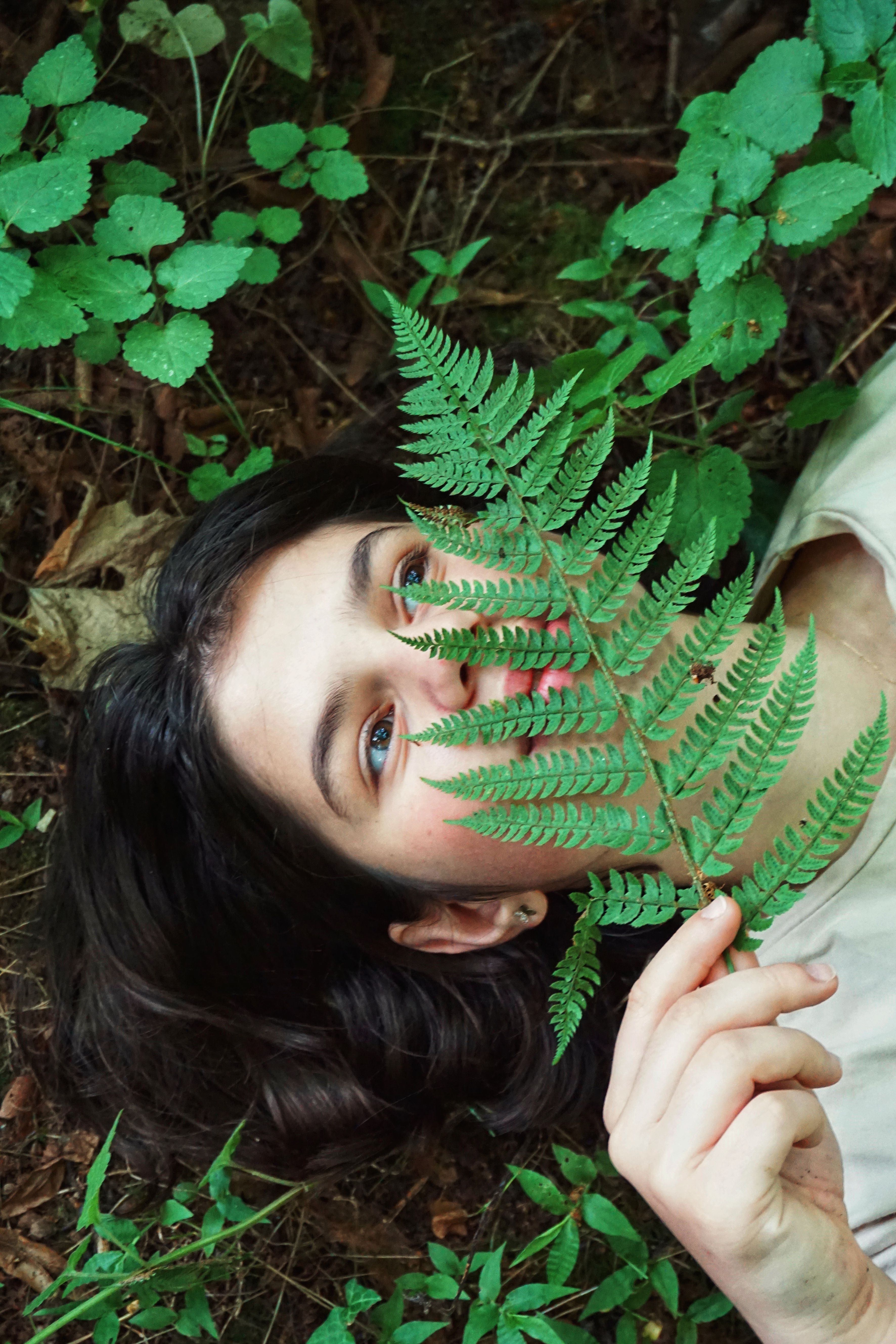 A young woman playfully holding a fern in a vibrant forest, surrounded by lush greenery.