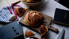 A rustic breakfast scene featuring fresh bread, eggs, and books on a wooden table.