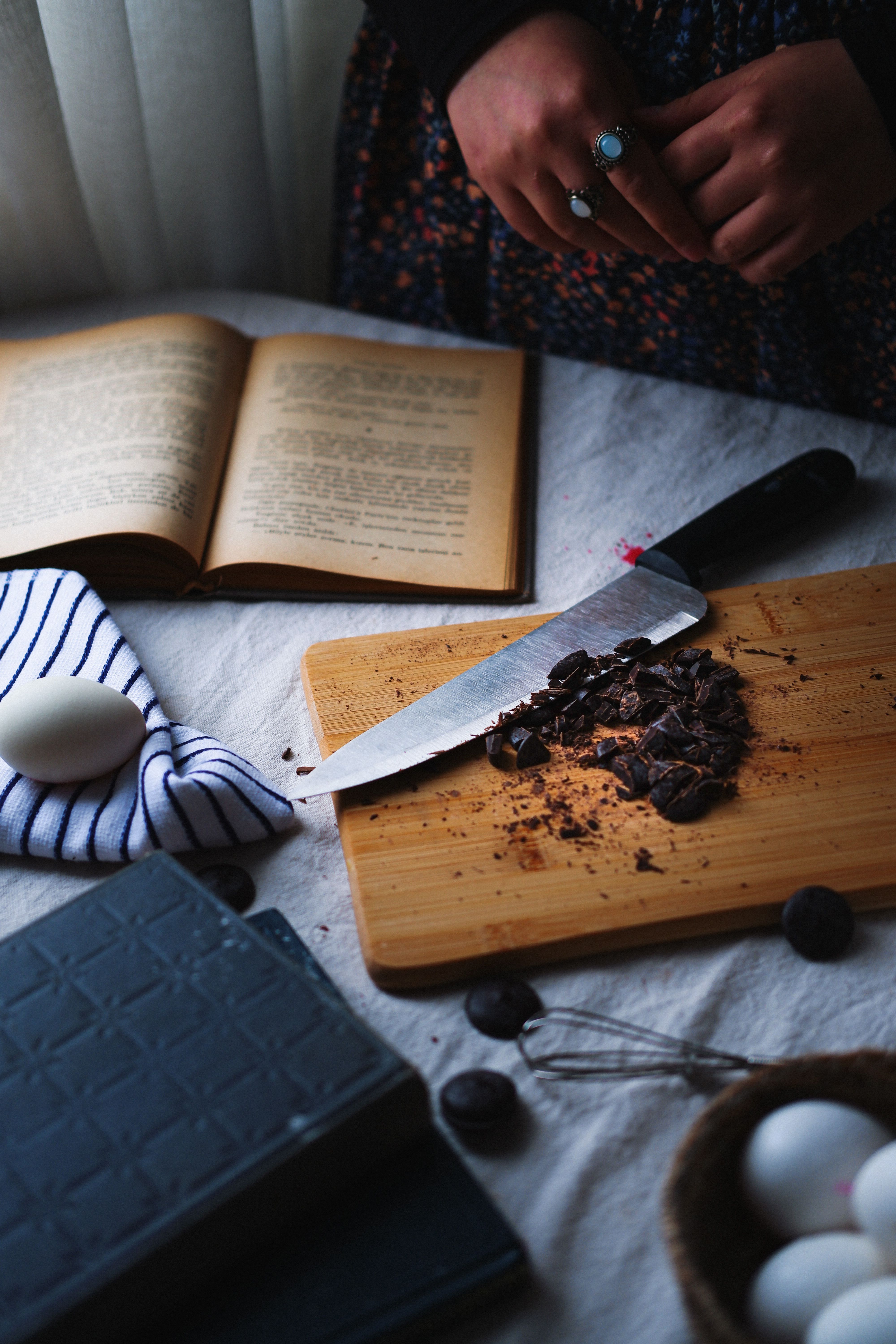 A warm kitchen setting with a cutting board, chocolate, eggs, and an open book.