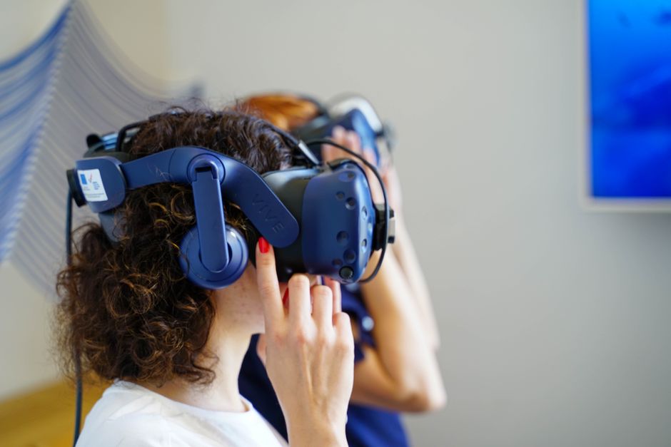 Two women using VR headsets, fully immersed in virtual reality technology indoors.
