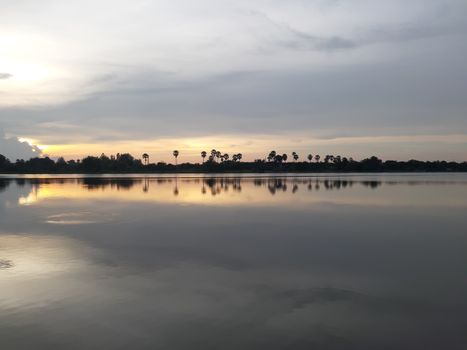 Tranquil view of sunset reflecting on a peaceful lake in Mueang Tai, Thailand.