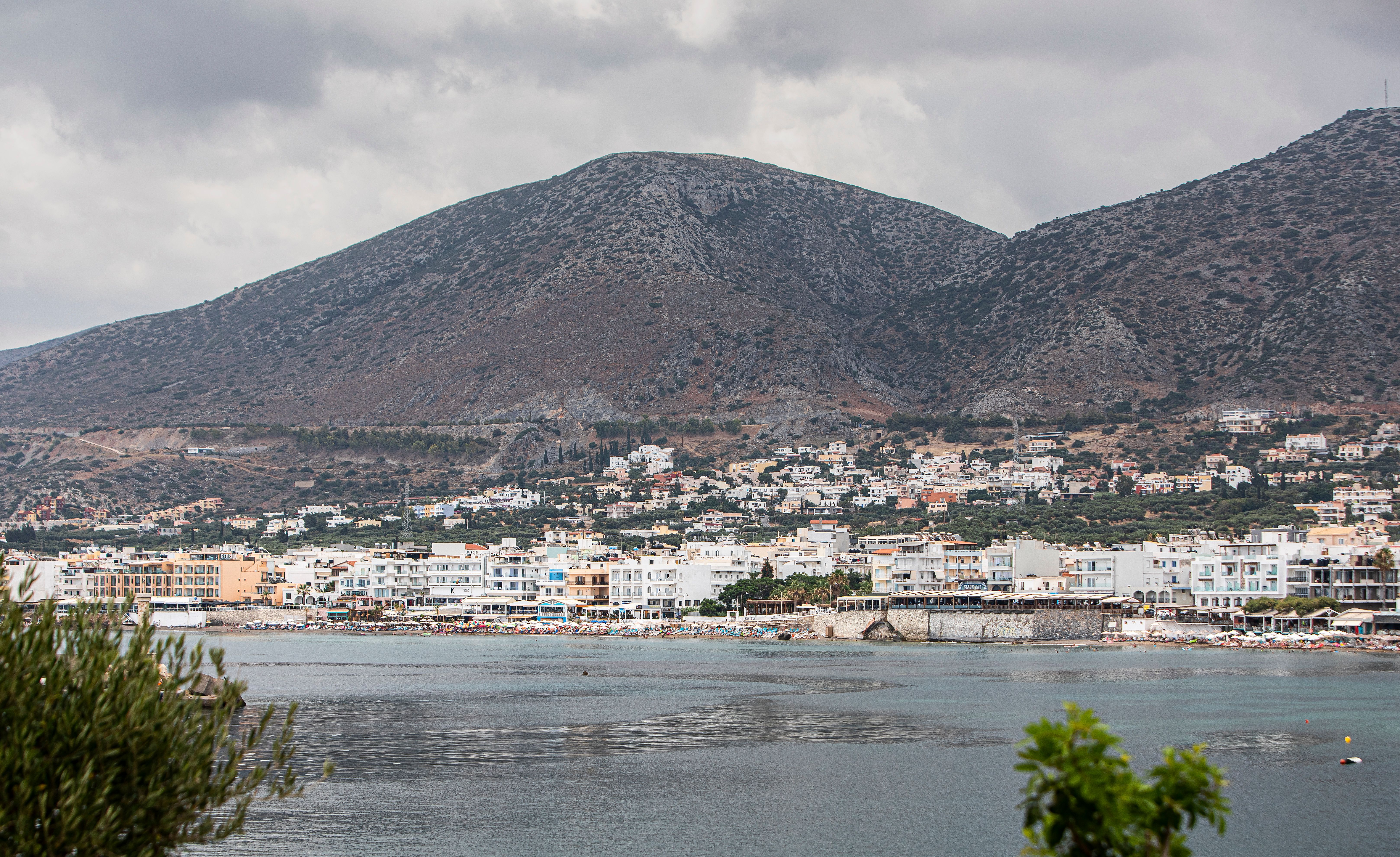 Charming coastal town with hills and sea under a cloudy sky.