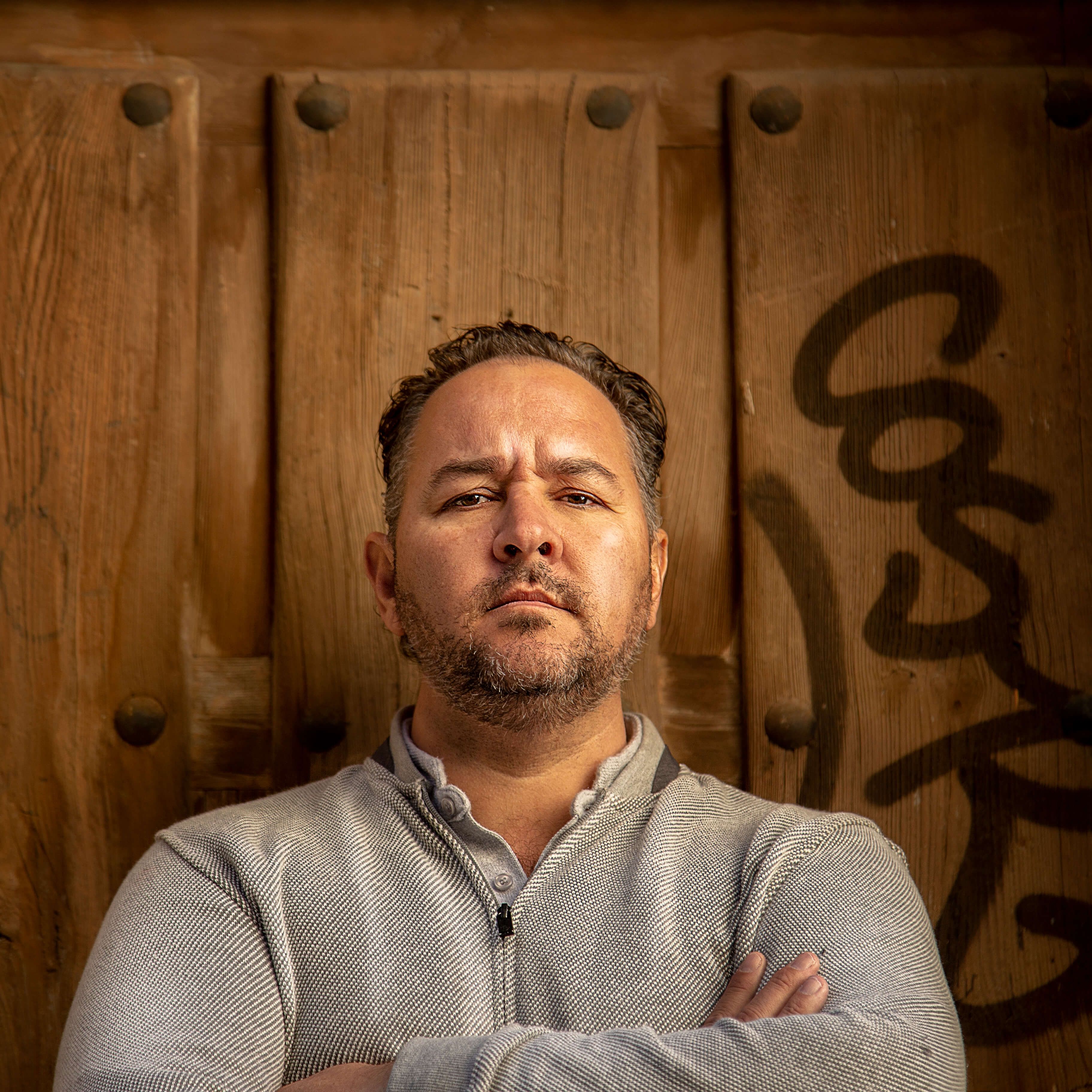 Portrait of a man with crossed arms and serious expression in front of a wooden door in Spain.