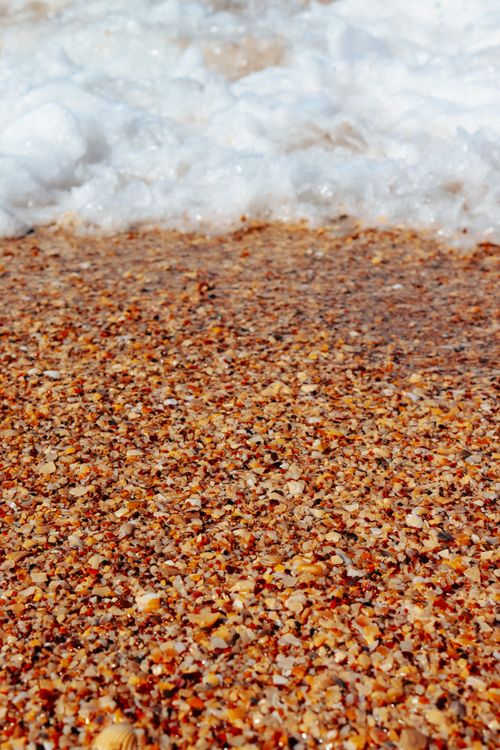 Free Close-up of vibrant pebbles with sea foam on a sandy beach. Stock Photo