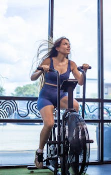 Young woman enjoying a vigorous workout on a stationary bike indoors with a vibrant, motivating atmosphere.