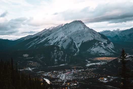A scenic view of a snow-covered mountain range and rural town under a cloudy sky.