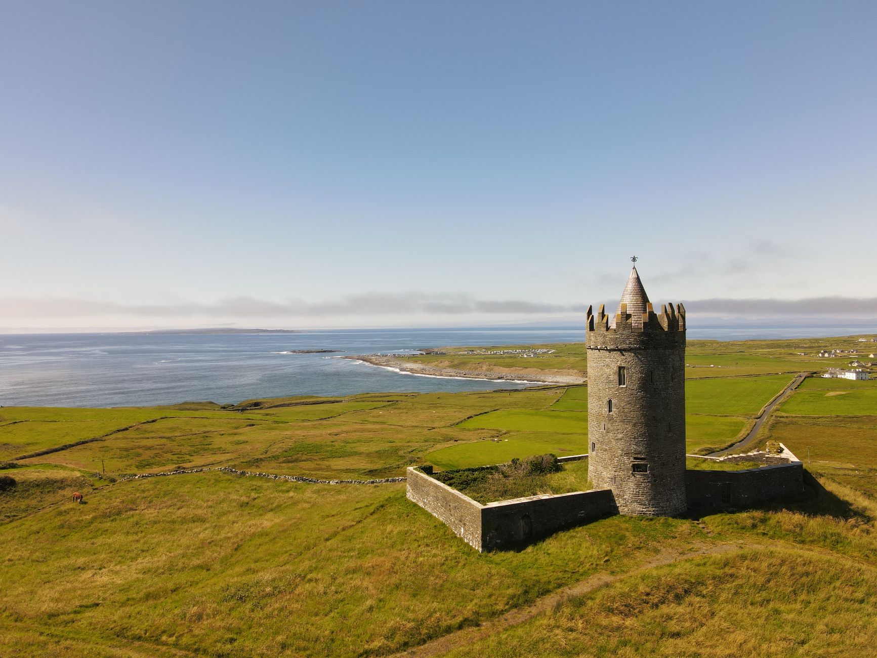 Aerial view of Doonagore Castle in County Clare, Ireland with vibrant green fields and ocean.