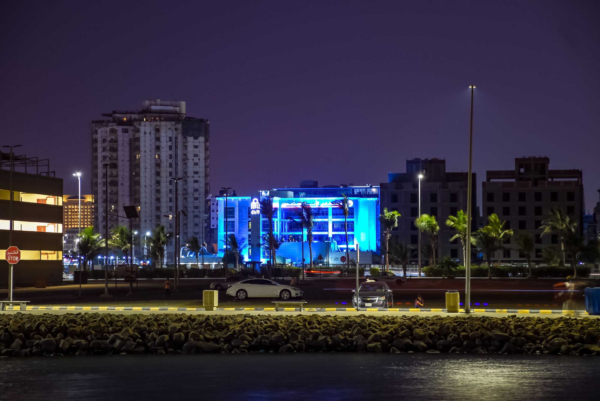 A vibrant city skyline illuminated at night featuring palm trees and modern architecture.
