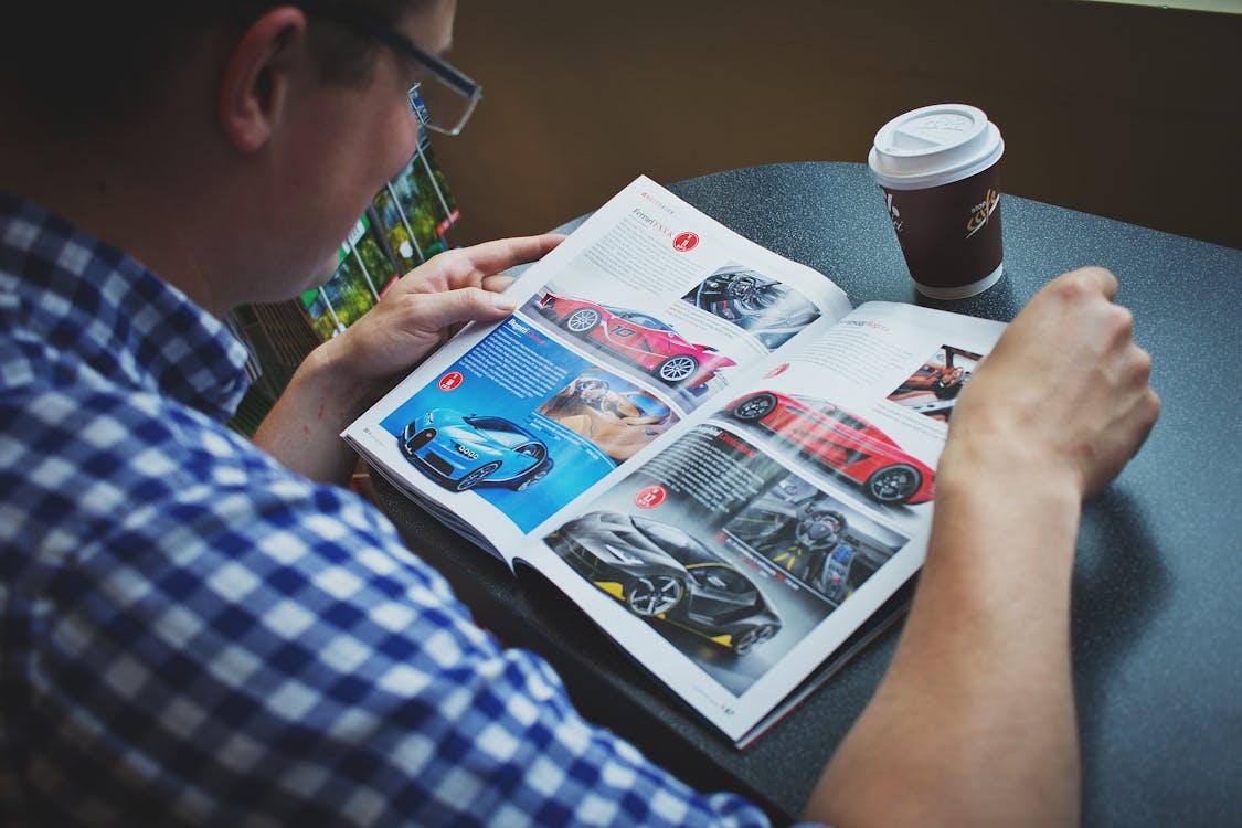 Free Man in Blue and White Gingham Print Shirt Reading Car Magazine Stock Photo