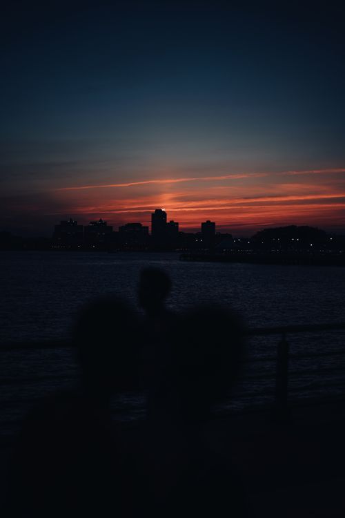 Free A tranquil dusk scene with silhouetted cityscape reflecting on the waterfront. Stock Photo