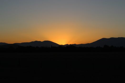 A tranquil sunset behind mountains with a vivid gradient sky and dark silhouettes.