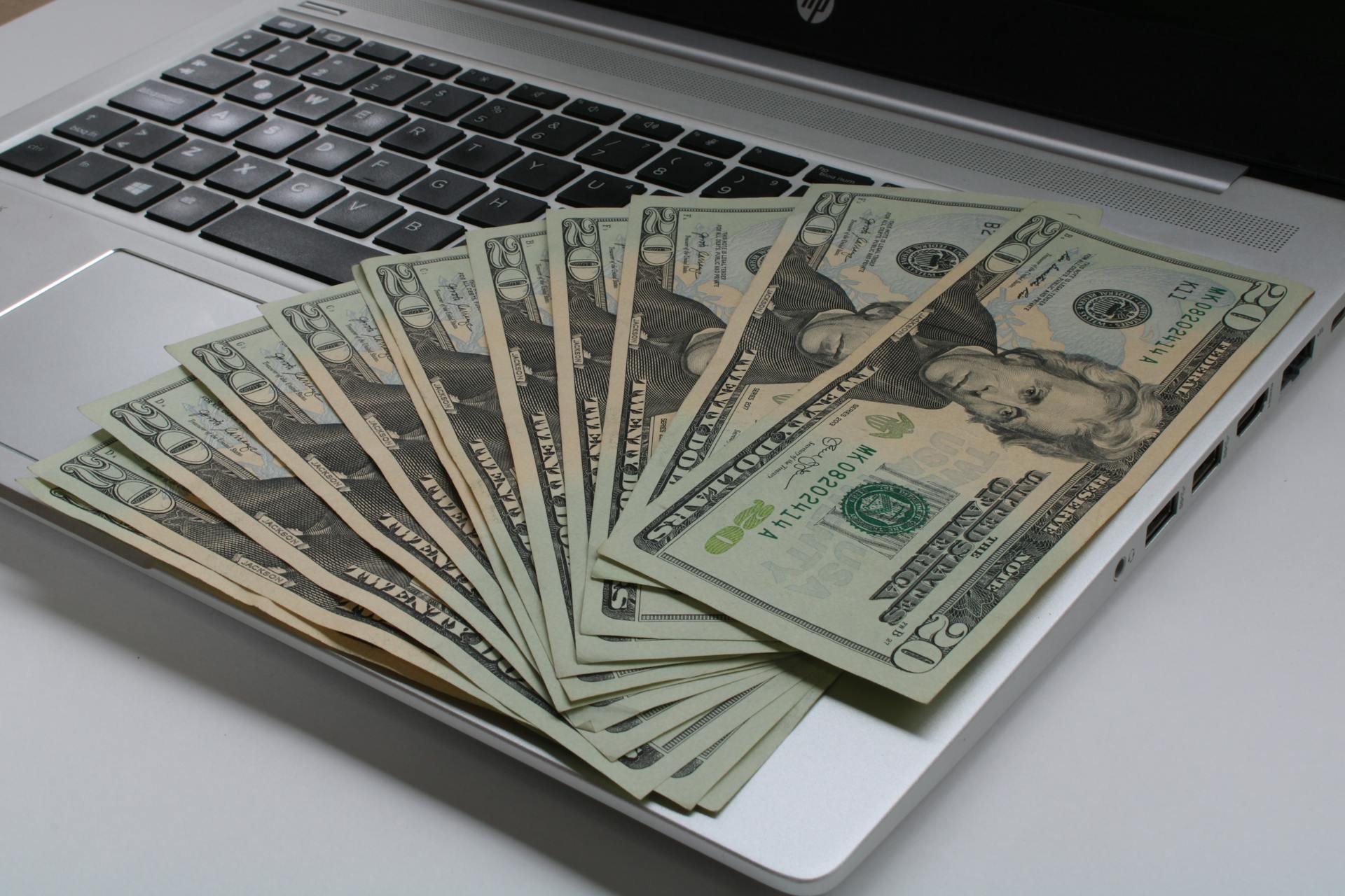 Stack of US dollar bills fanned out on a laptop keyboard, symbolizing online finance.