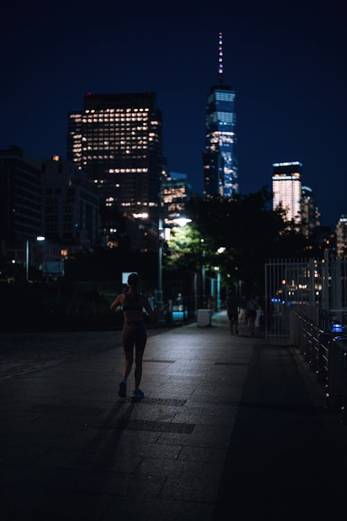 Man in Black T-shirt Walking on Sidewalk during Night Time