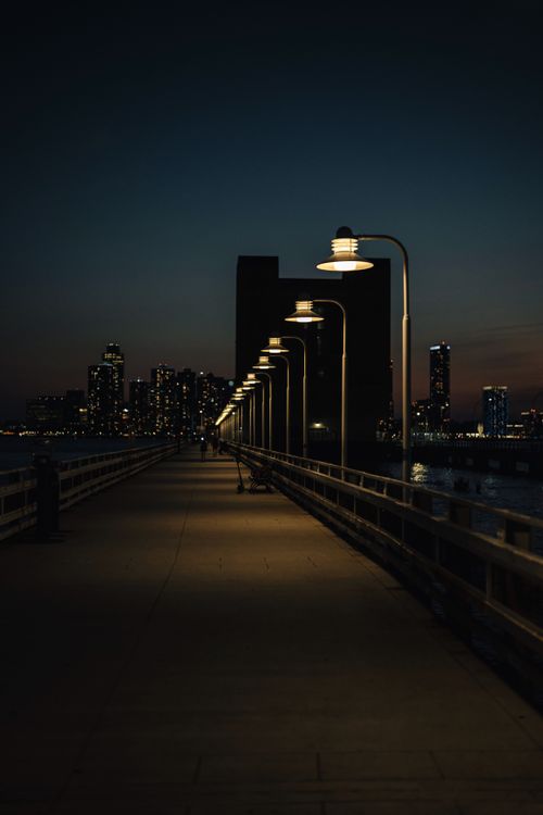 Free A serene nighttime view of a city with an illuminated pier leading into the darkness. Stock Photo