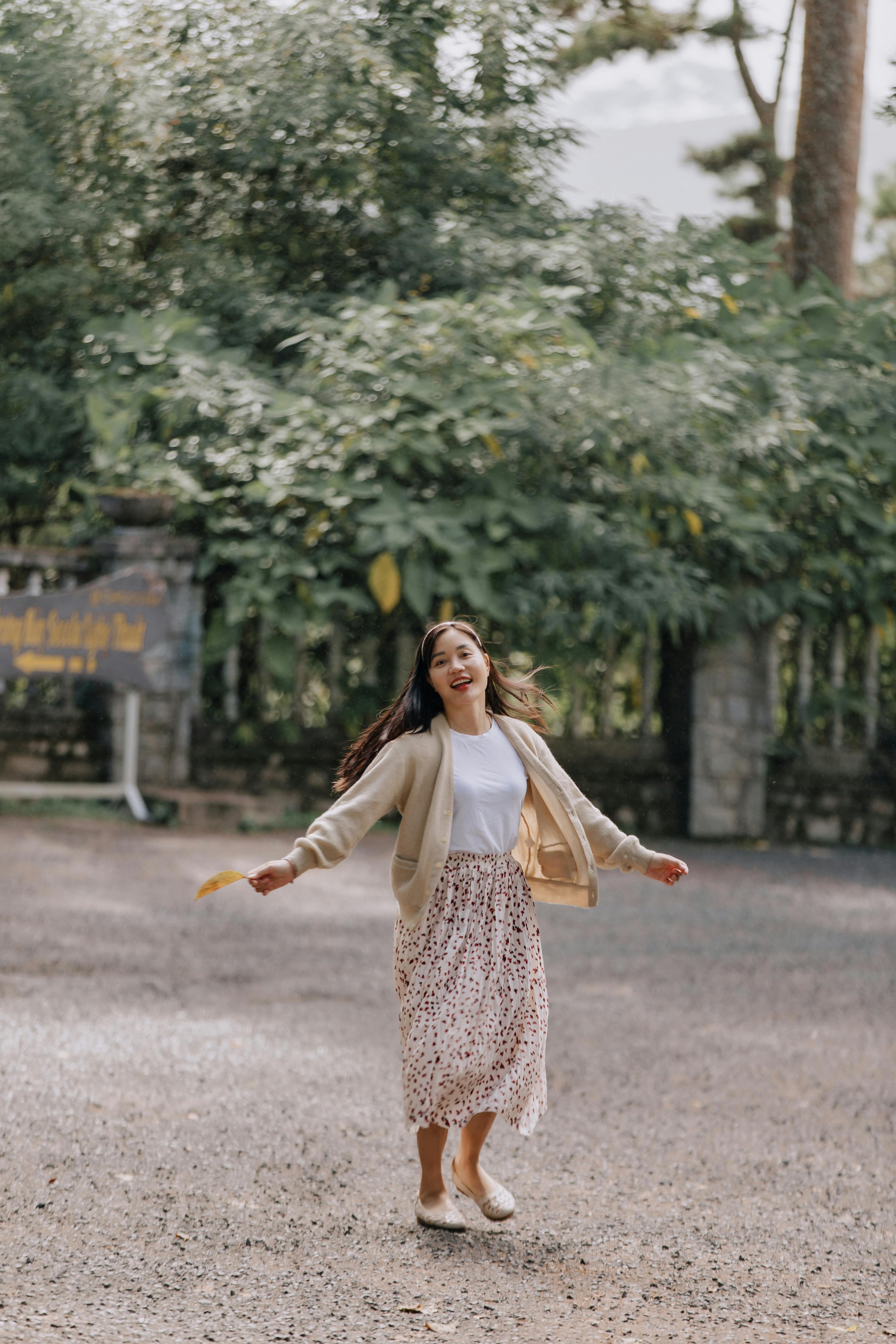 woman in white long sleeve shirt and brown and white floral skirt standing on gray concrete