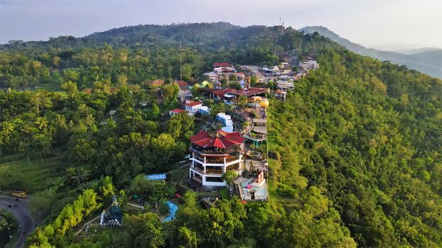 Aerial view of a lush hillside village in Yogyakarta, Indonesia, surrounded by dense greenery.
