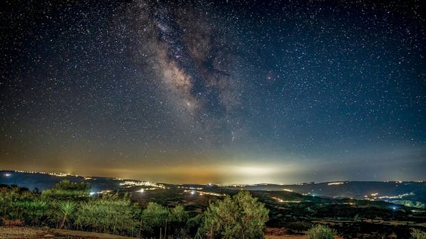 A breathtaking view of the Milky Way galaxy shining over a night landscape with distant city lights.