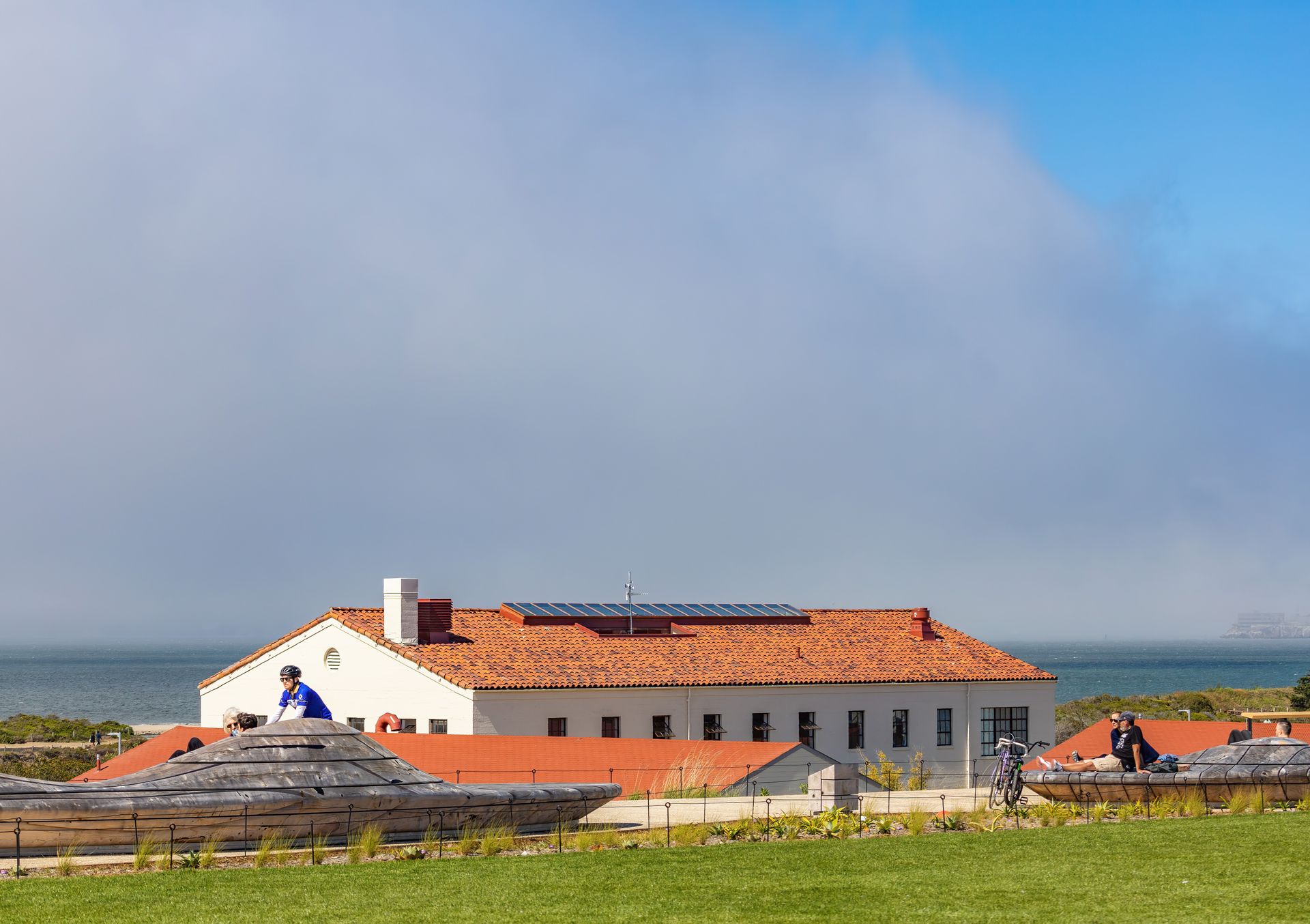 Coastal building with solar panels, people enjoying outdoor activities by the sea.