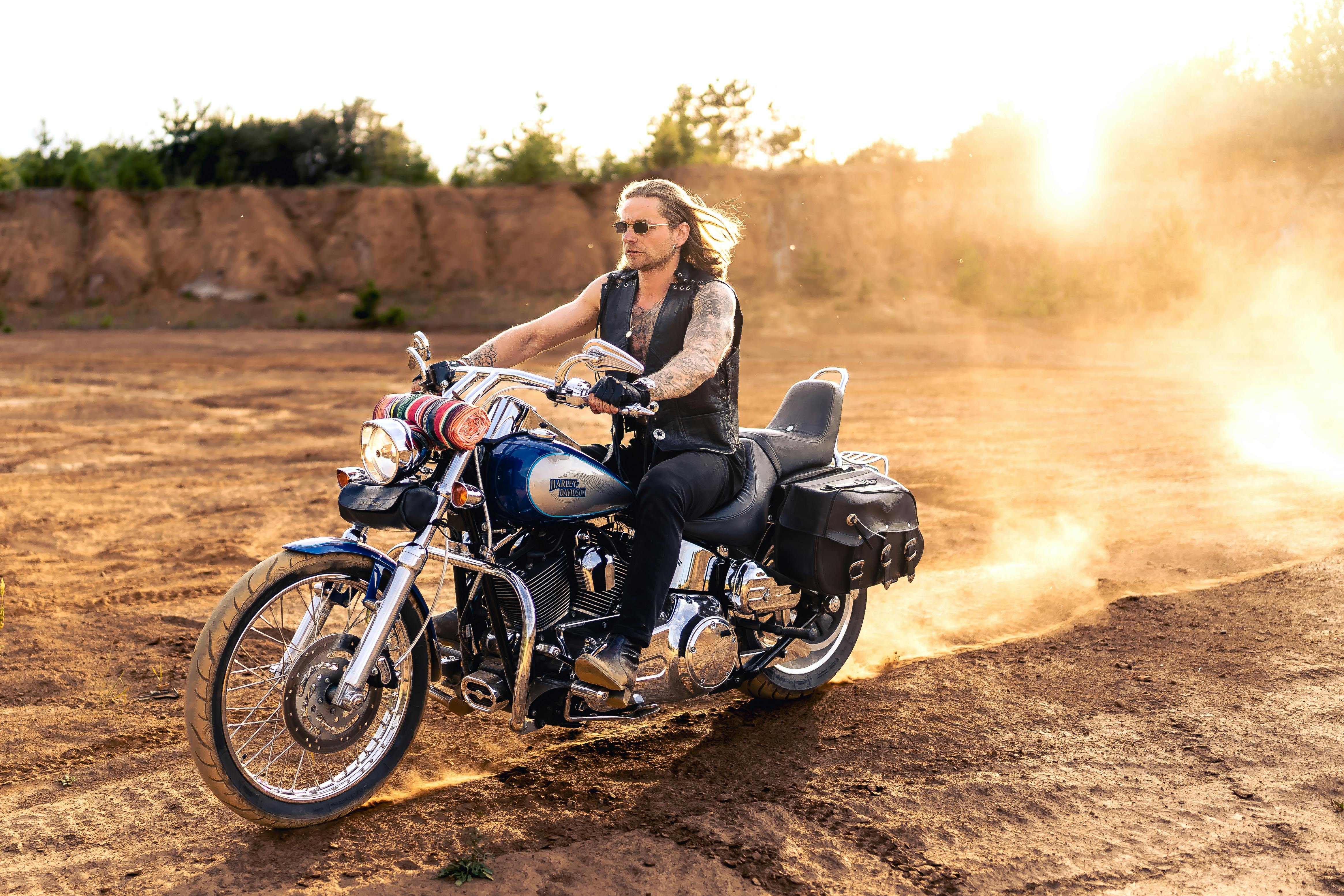 A tattooed man riding a classic motorcycle on a dusty dirt road in Slovakia.