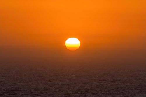 Free Captivating view of the sun setting over the ocean with a golden sky. Stock Photo