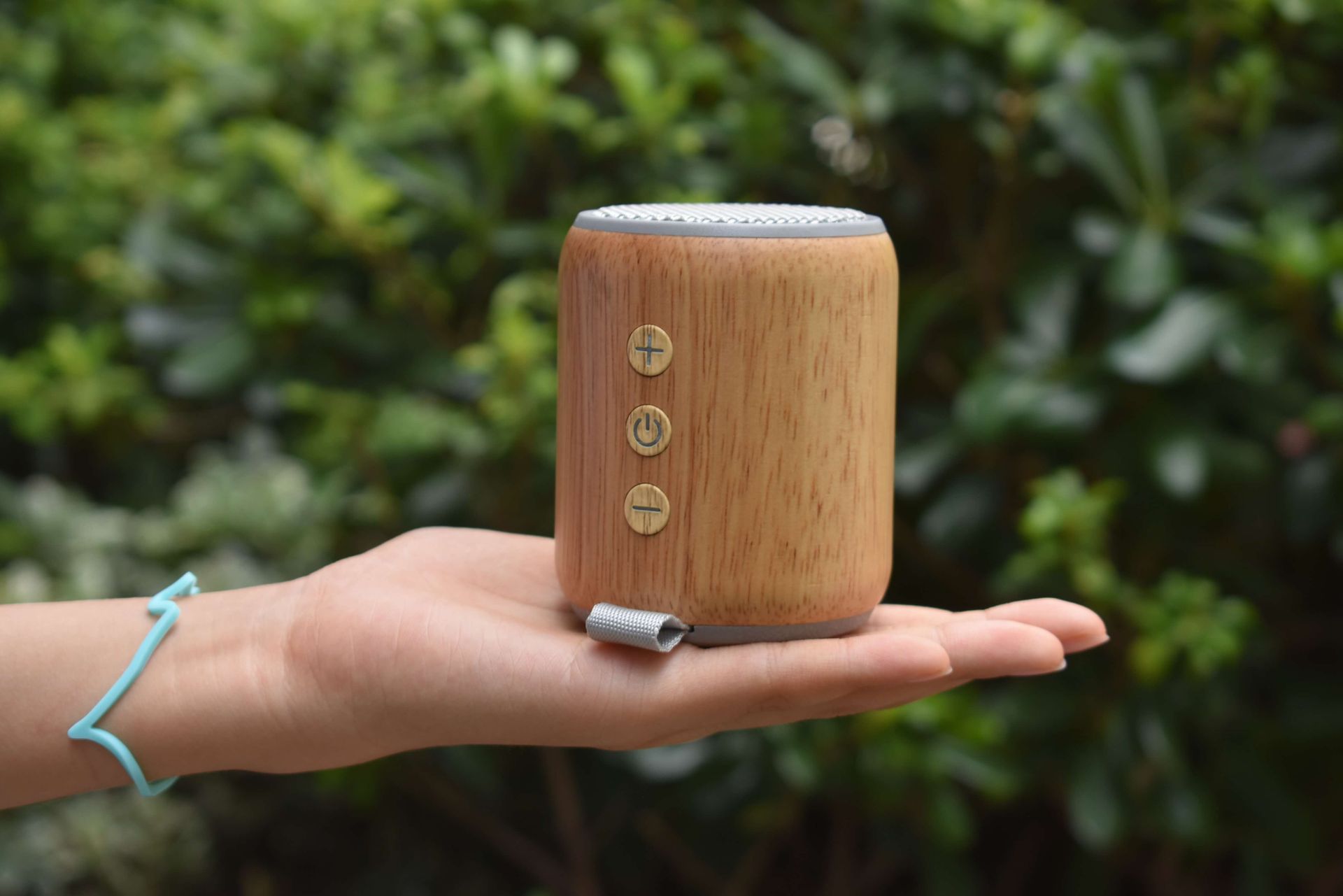 Portable wooden speaker with eco-friendly design held outdoors in a hand, offering a natural aesthetic.