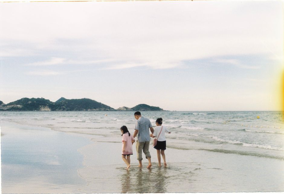A father and two children enjoy a peaceful walk along the serene beach shoreline.