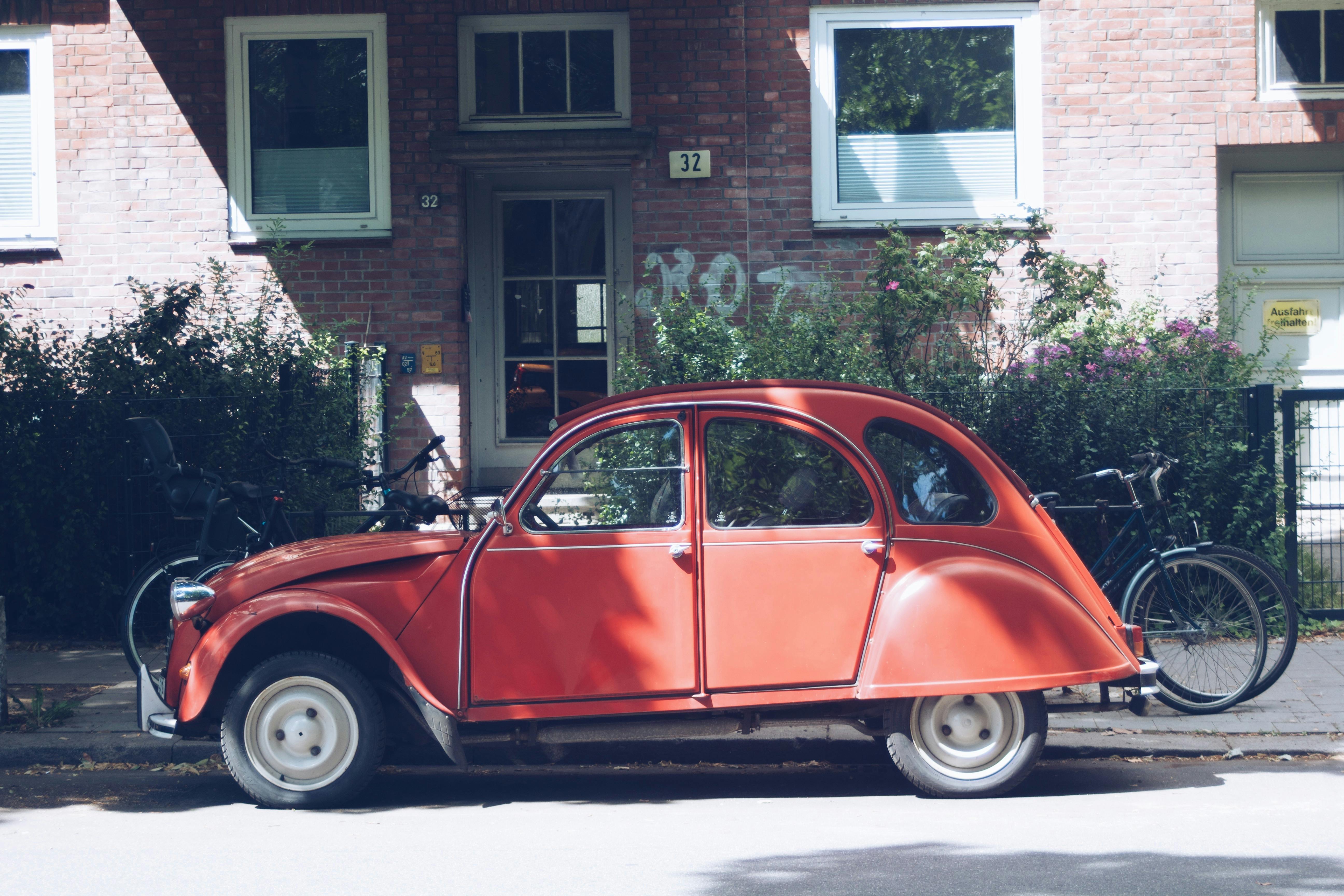 red volkswagen beetle parked beside brown brick building