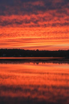 A striking sunset reflecting over a calm lake near Quebec City, Canada, with vibrant colors in the sky.