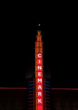 Brightly lit Cinemark sign glowing against a dark night sky with a crescent moon.