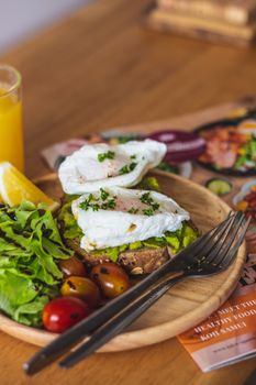 Delicious avocado toast topped with poached eggs, served with fresh salad and cherry tomatoes.