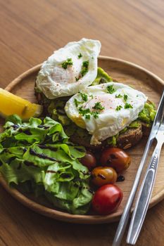 Delicious poached eggs on avocado toast with cherry tomatoes and fresh lettuce.