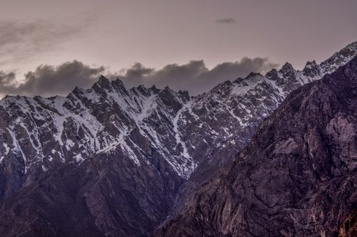 Free Snowcapped rugged mountain peaks under dramatic clouds at dusk, showcasing raw natural beauty and serenity. Stock Photo