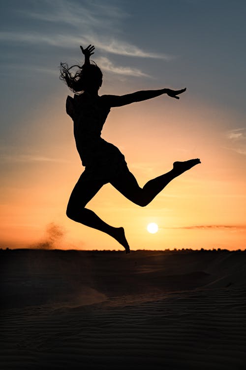 Silhouette of Woman Jumping on Beach during Sunset