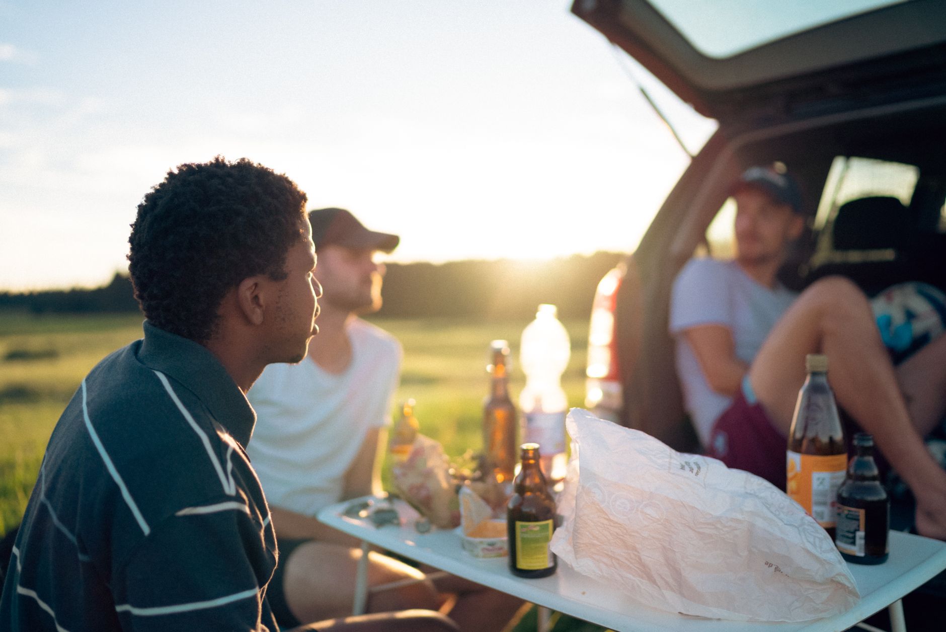 A group of friends enjoying a picnic with drinks and snacks at sunset. Perfect summer leisure time.