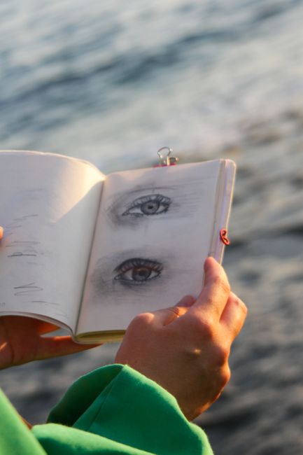Hands holding an eye sketchbook with a blurred ocean background, sunny day. Hands holding an eye sketchbook with a blurred ocean background, sunny day.