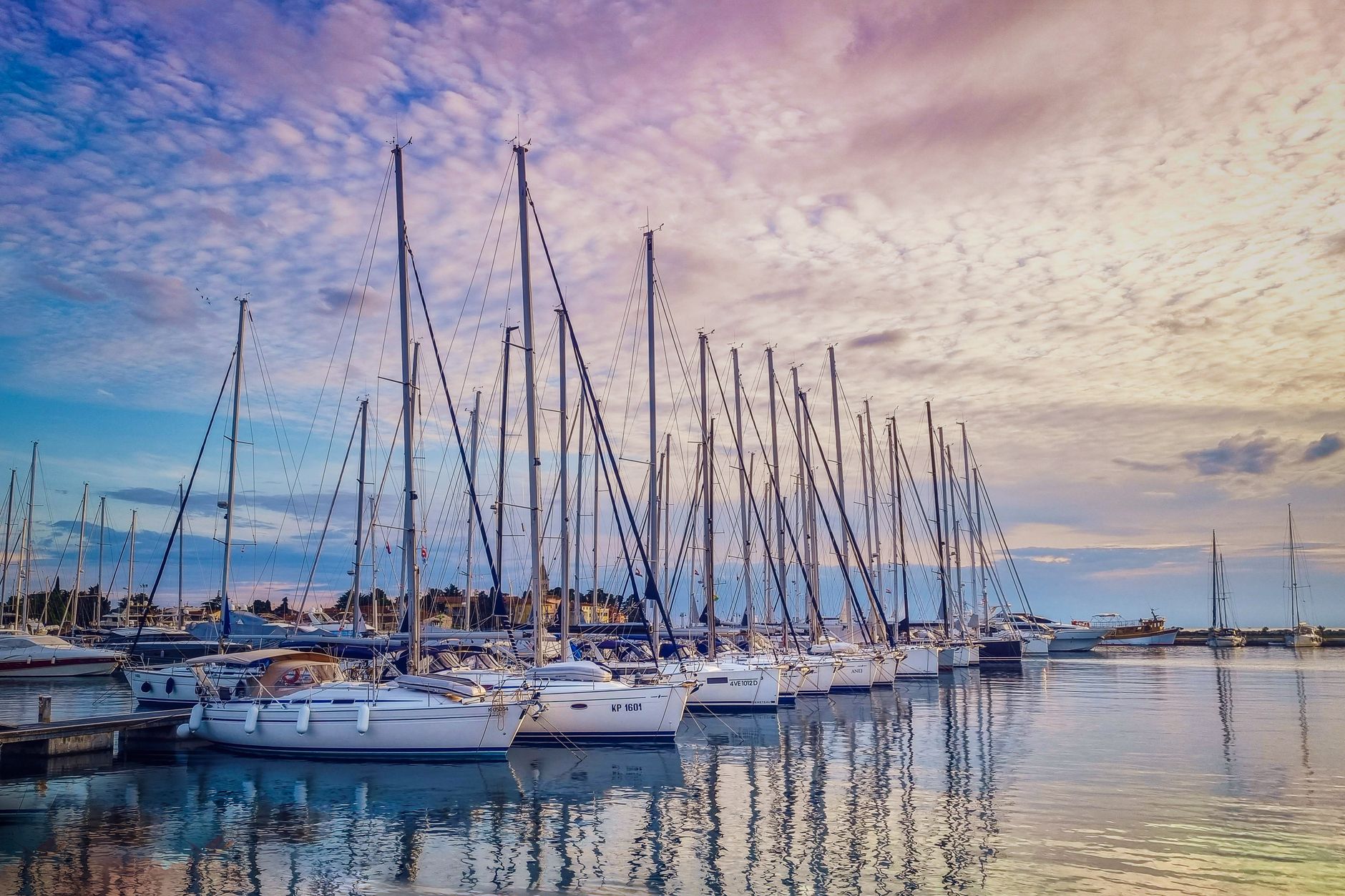 Tranquil marina with docked sailboats reflecting on the water at sunset, featuring a colorful sky.