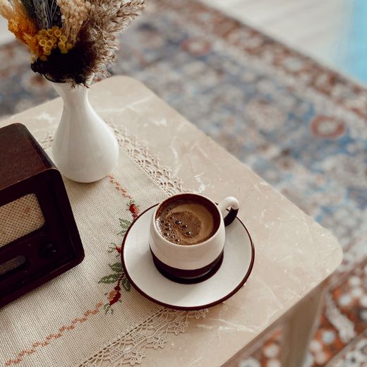 Cup and saucer beside a white vase of dried flowers — photo by Sena on Pexels