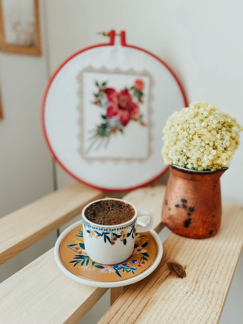 Free Stylish coffee setup with floral embroidery and rustic vase on a wooden surface. Stock Photo