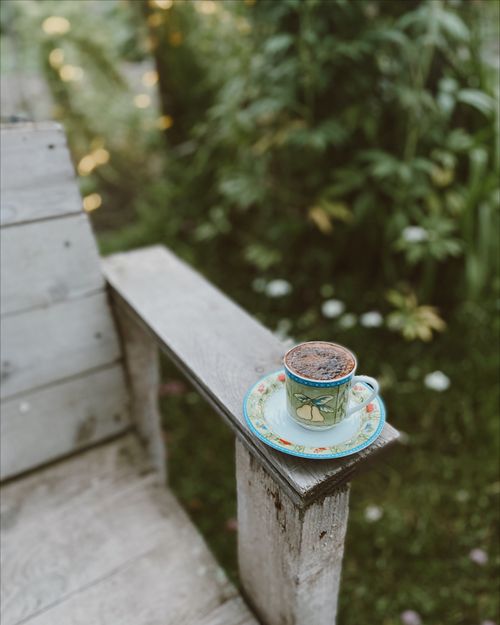 Free A beautifully patterned coffee cup on a wooden armrest surrounded by lush greenery. Stock Photo