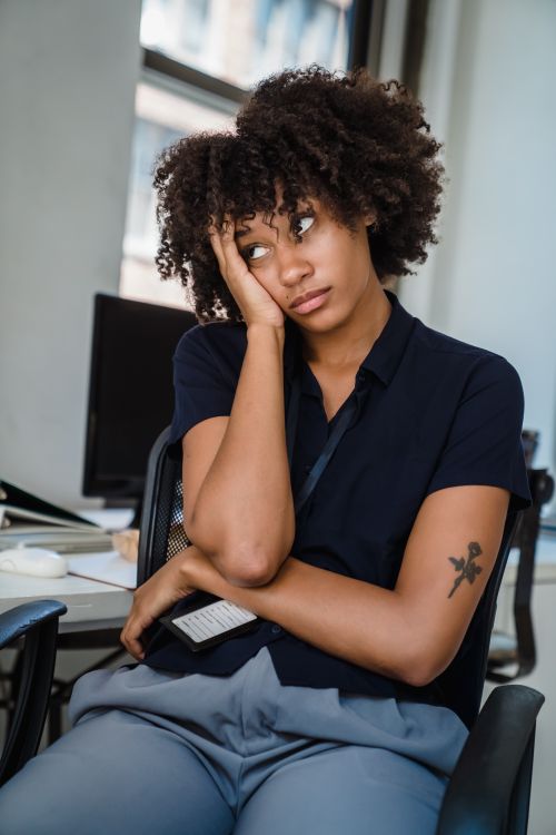 Free A woman with an afro hairstyle looking exhausted while sitting in an office setting. Stock Photo