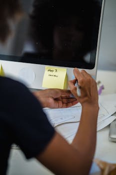 Close-up of a woman writing on sticky notes in an office setting.