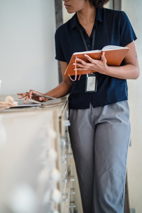 Woman Using a Laptop and Holding a Notebook