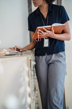 Businesswoman standing by a desk in an office holding a notebook, deep in work.