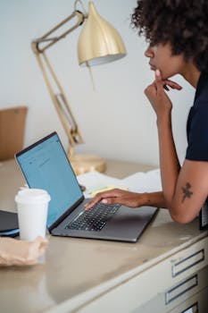 Young woman concentrates while working on a laptop at a stylish desk setup.