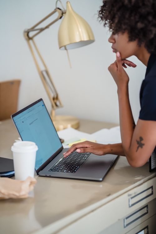 Free Young woman concentrates while working on a laptop at a stylish desk setup. Stock Photo