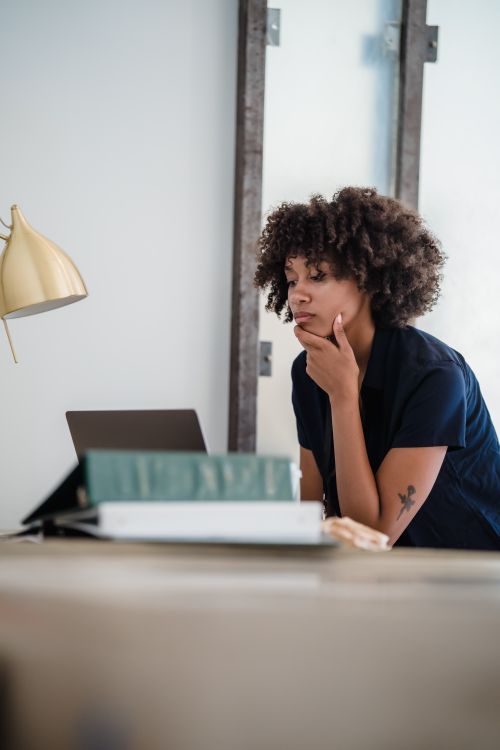 Free African American woman contemplating work at a desk in an office environment. Stock Photo