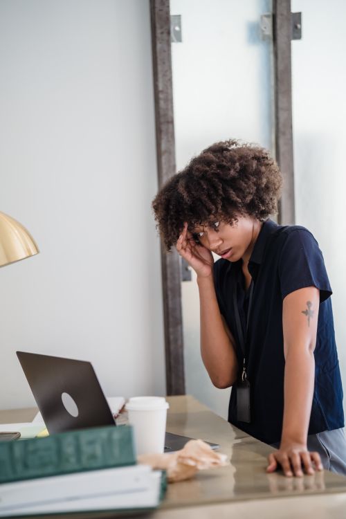 Free Businesswoman overwhelmed with work, standing at her desk in an office setting. Stock Photo